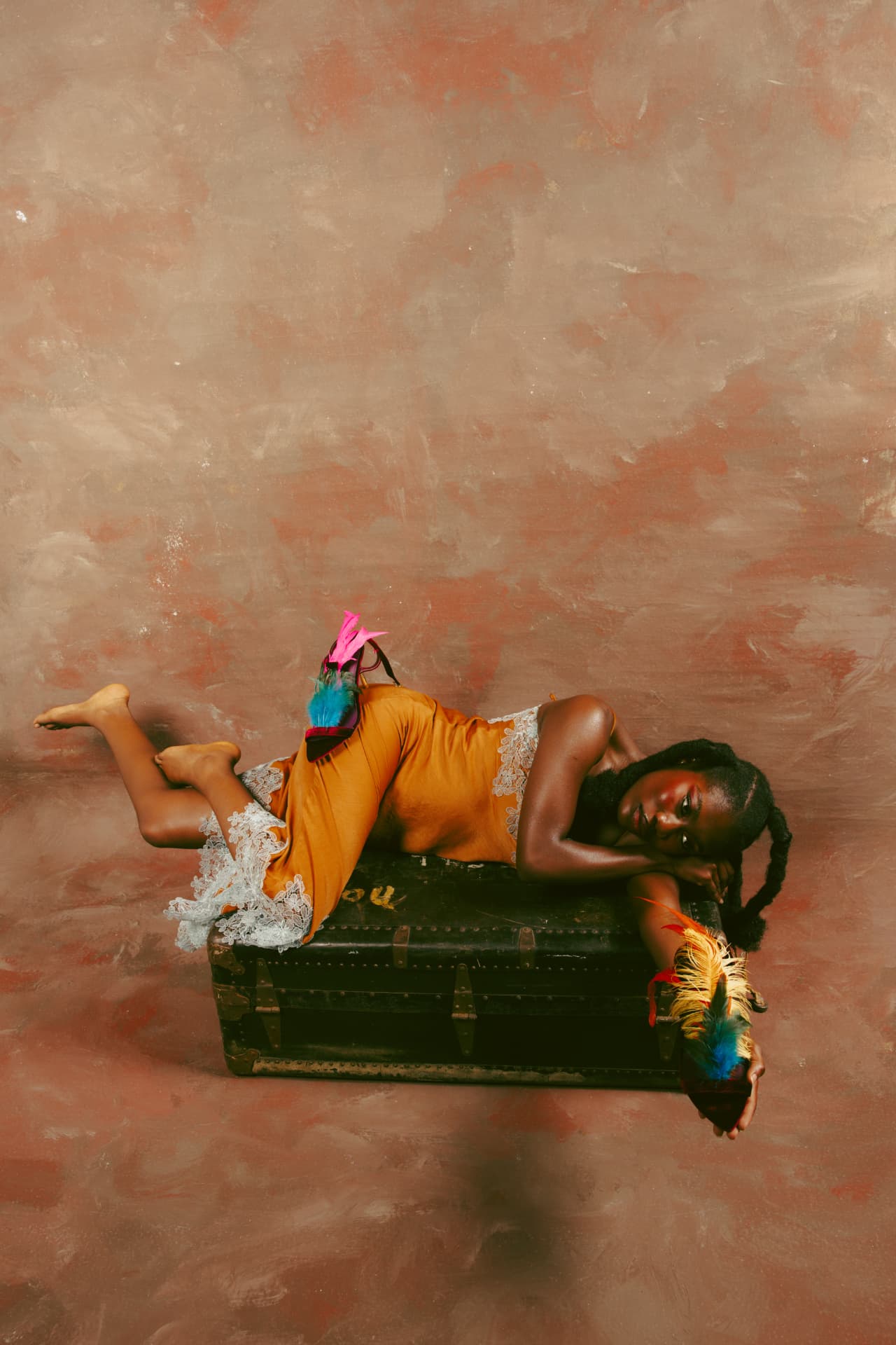 Model reclining on a vintage trunk with feathered heels